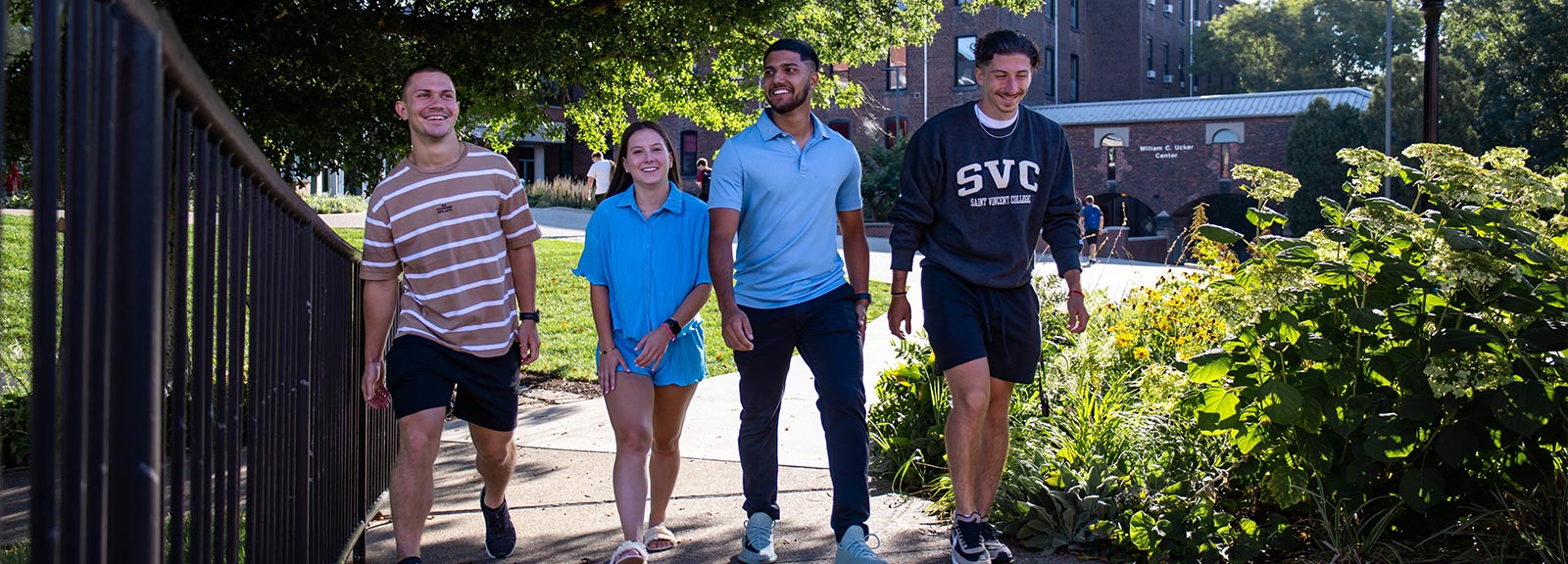 A photo of four diverse college students walking together on campus, smiling and engaging with each other.