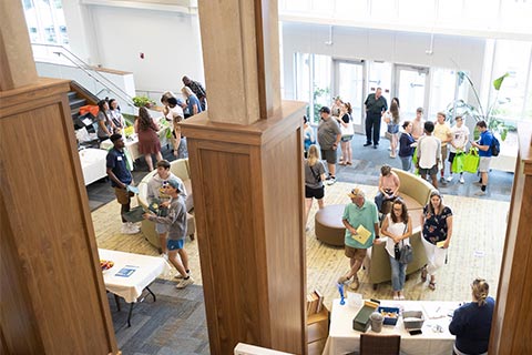 A bustling community event in a spacious hall with attendees engaging at various tables and seated areas.