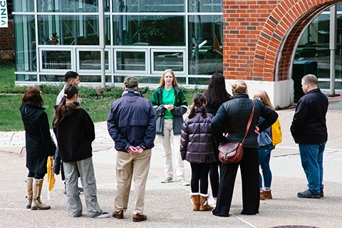 A group of people gathered around a tour guide outside a building, listening attentively.