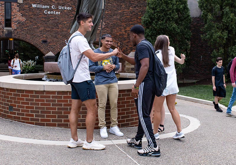 A group of diverse college students engaged in a friendly conversation near a fountain at William C. Ucker Center.
