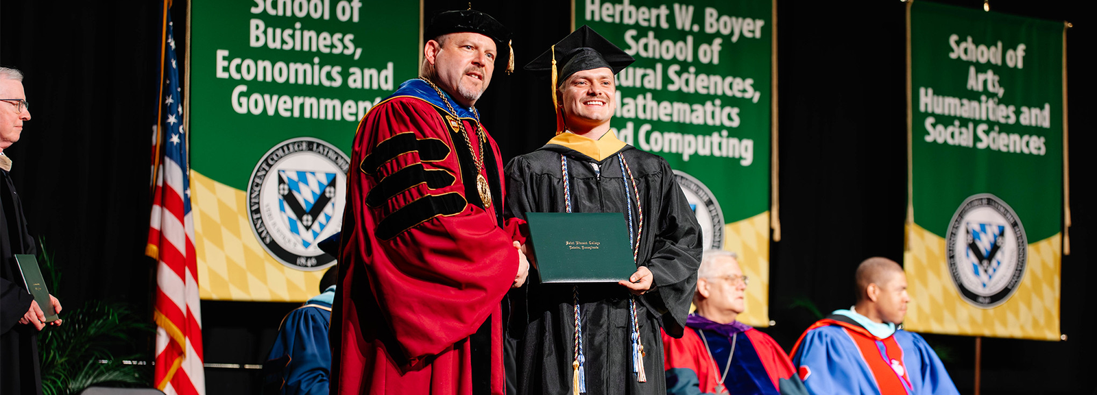 Saint Vincent President Father Paul Taylor poses with a male graduate receiving his diploma 