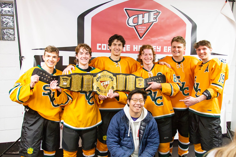 Saint Vincent players (left to right) Conner Fauth, Caden Horton, Luca Rosato, Jacob Holtzman, Michael Ridilla and Zachary Ridilla celebrate with an unidentified friend (front row, center) after winning the College Hockey East MD3 championship belt.