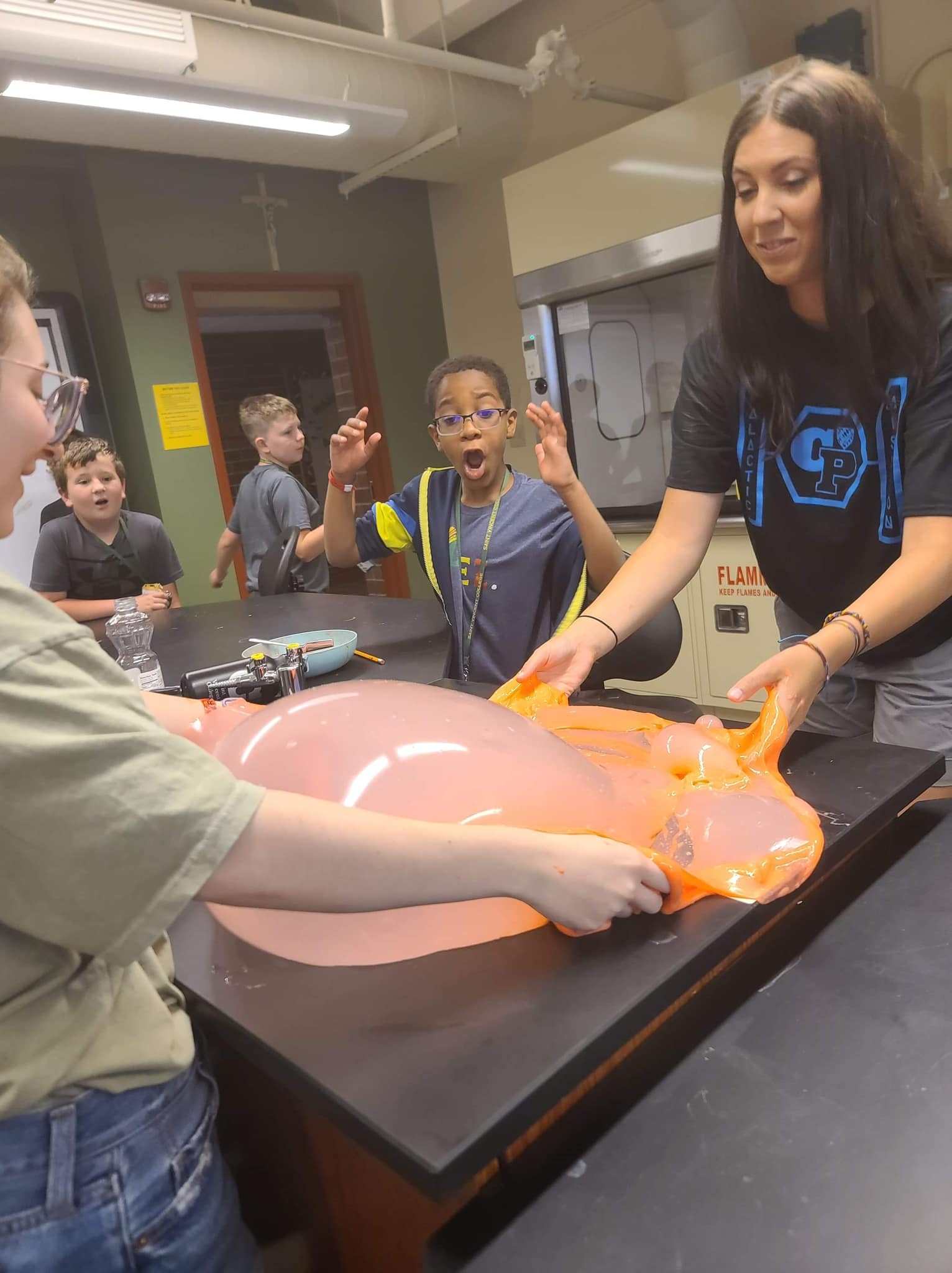 Children observing an interactive science demonstration as a colorful balloon-like object is being manipulated by an instructor.