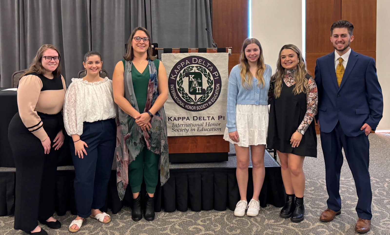 Group of six students standing in front of a Kappa Delta Pi banner at an education honor society event.