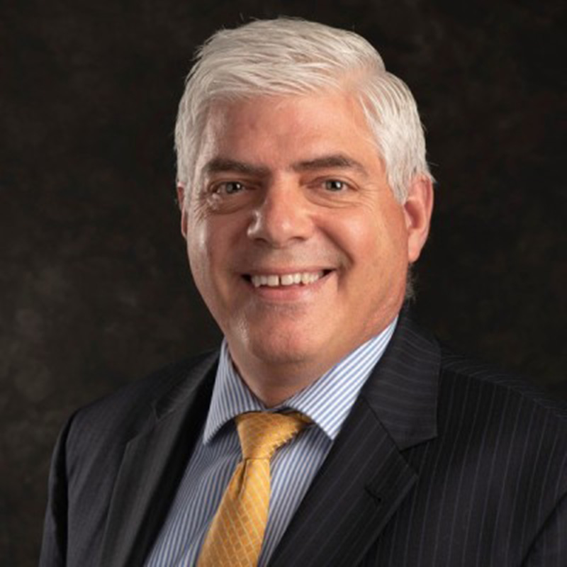 Professional headshot of a smiling man in a suit with a yellow tie.