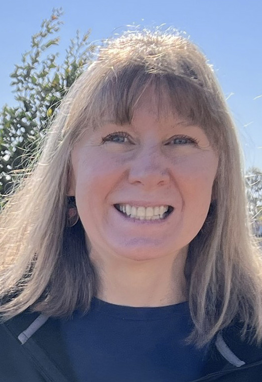 Smiling woman with shoulder-length hair outdoors on a sunny day.