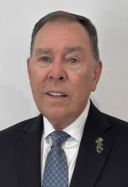 Professional headshot of a man wearing a suit and tie, with a pin featuring the letters "SVC" on his lapel.