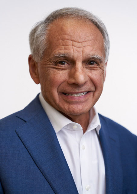 Smiling man in a blue suit and white dress shirt against a plain light background.